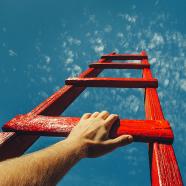 Hand Reaching For Red Ladder Leading To A Blue Sky