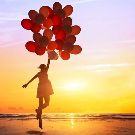 happiness or dream concept, silhouette of happy woman jumping with multicolored balloons at sunset on the beach
